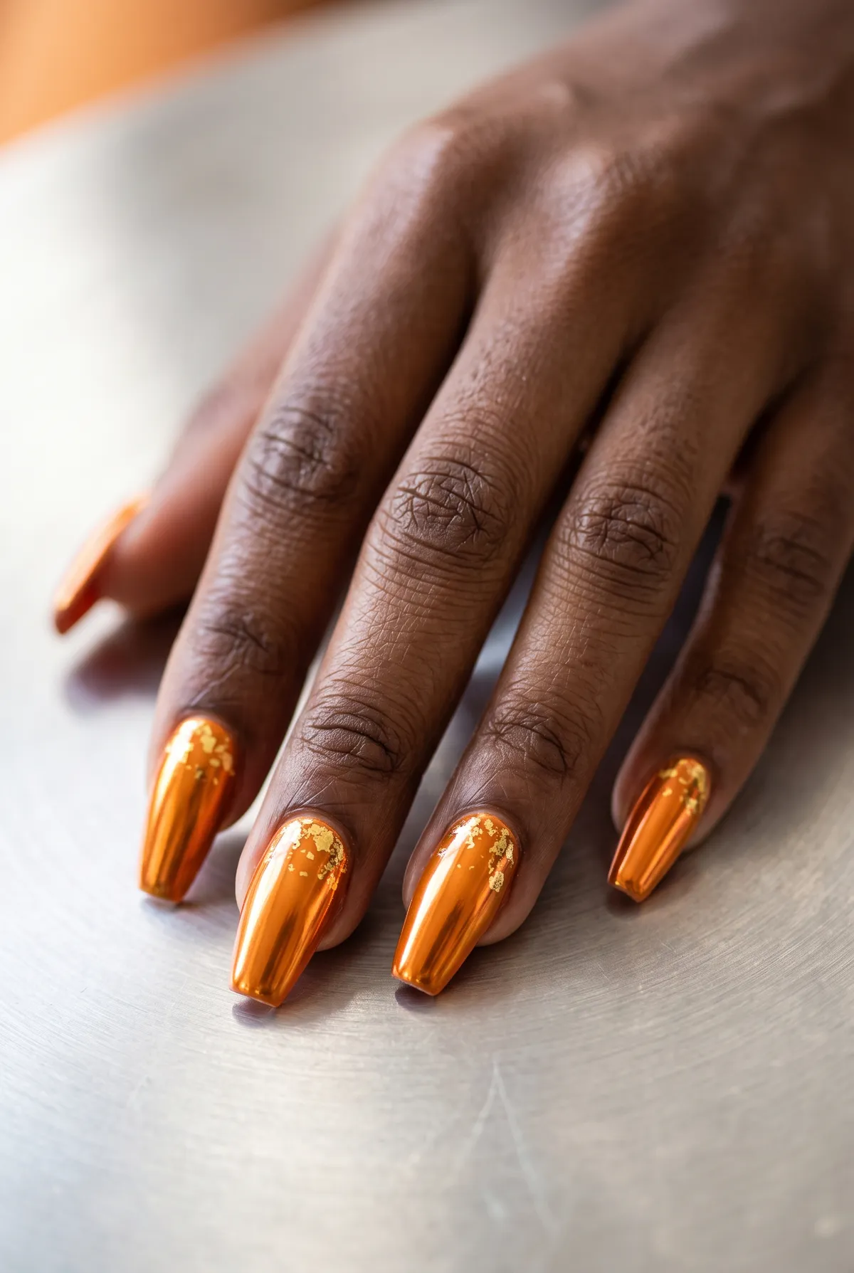 Pumpkin Chrome Coffin — coffin halloween nails with orange chrome powder over a coffin-shaped gel base with a scattering of gold foil flecks…